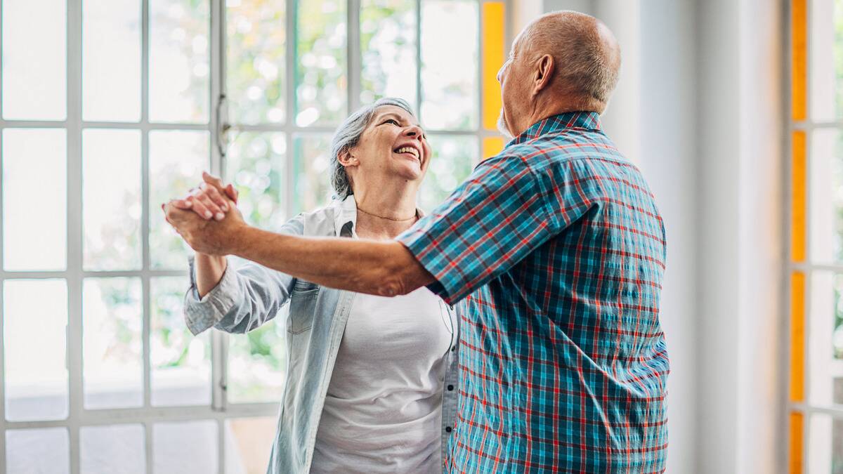 A couple dancing in their home, both smiling at one another.