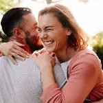 A couple hugging outside, both smiling, the woman with her eyes closed as they both hang on tightly.