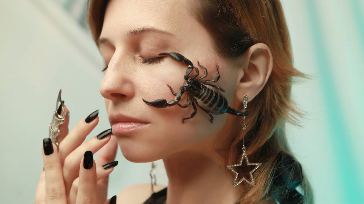 A woman with a scorpion crawling on her face, her eyes closed, looking poised and peaceful.