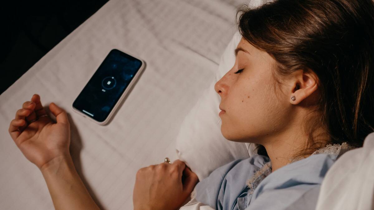 A close shot of a woman sleeping in bed, laying on her side, her phone on the bed next to her pillow.