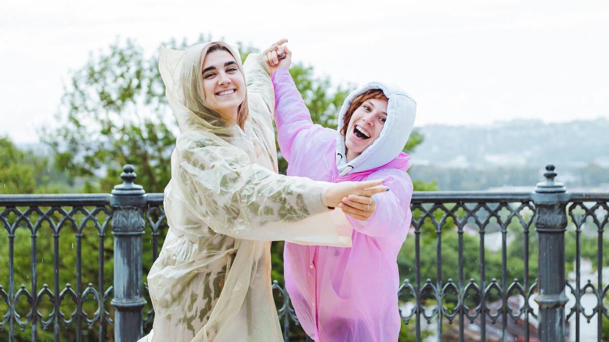 Two friends in rain coats smiling and dancing outside.