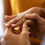 A close photo of a man putting a ring on his girlfriend's finger.