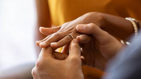 A close photo of a man putting a ring on his girlfriend's finger.