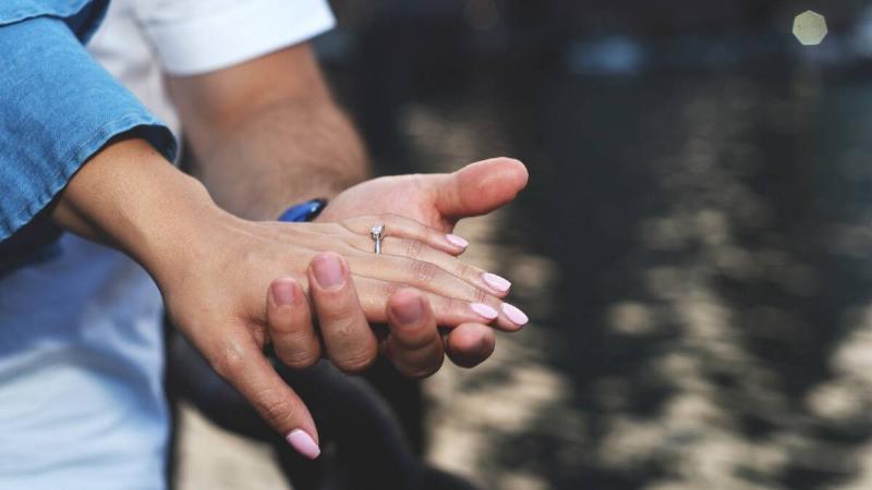 A man holding his girlfriend's hand, showing off her engagement ring.