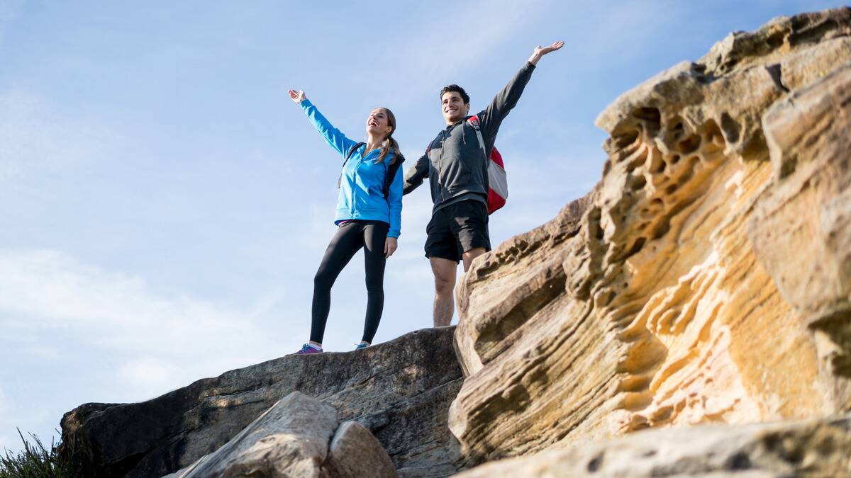 A couple standing on a rock face together, having just climbed or hiked it, both with an arm in the air in victory.