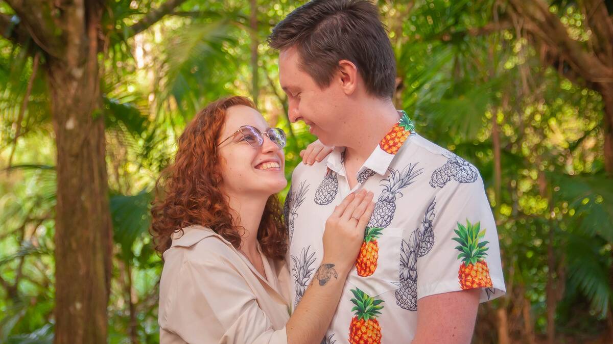 A couple standing outside, the woman leaning against the man, a hand on his chest, looking up at him as they smile at one another.