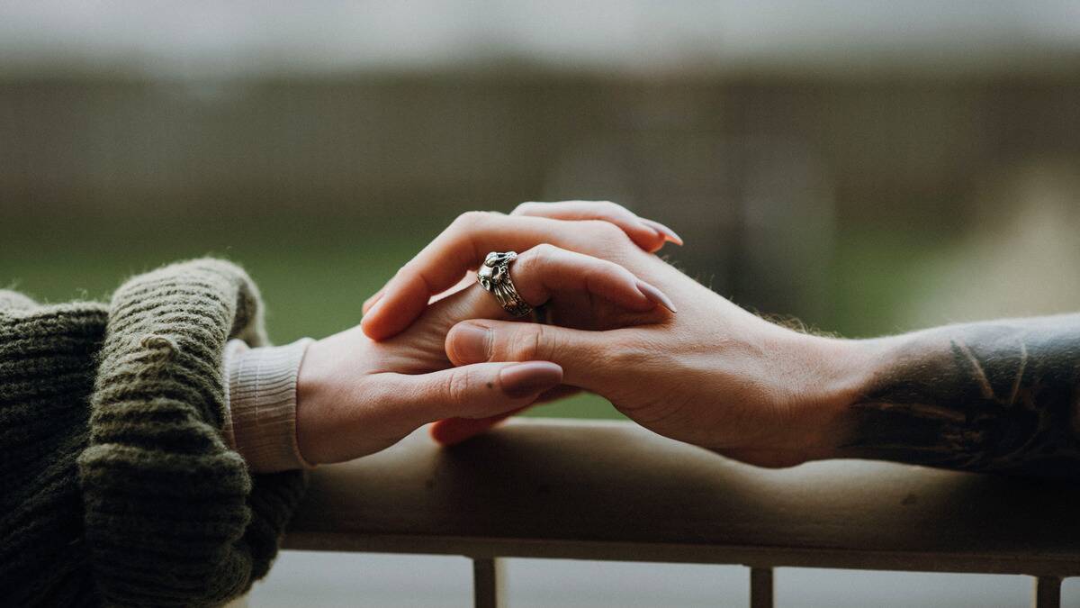 A close shot of two different hands with their fingers interlaced as they rest on a railing.