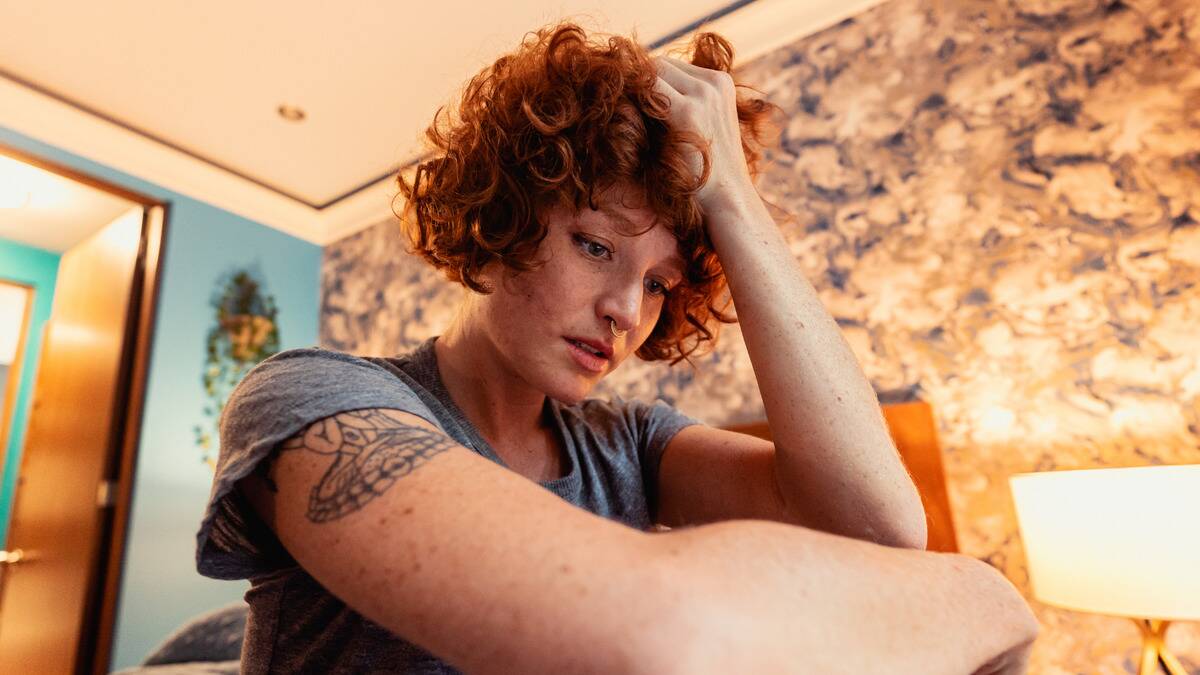 A low-angle shot of a young person who has their hand in their hair, looking down at the ground anxiously.