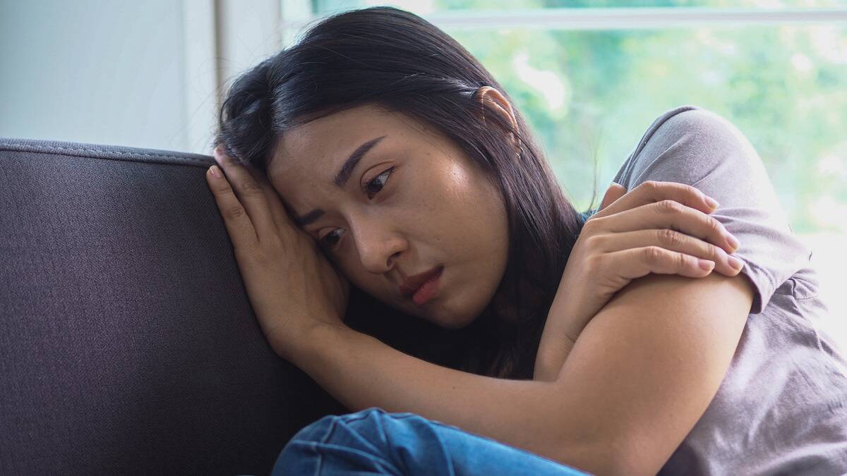 A close shot of a woman curled up on her couch, resting her face on her hand, looking sad.