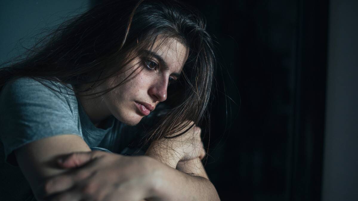 A close shot of a woman sitting and leaning forward with her arms folded, looking ahead with an empty expression.