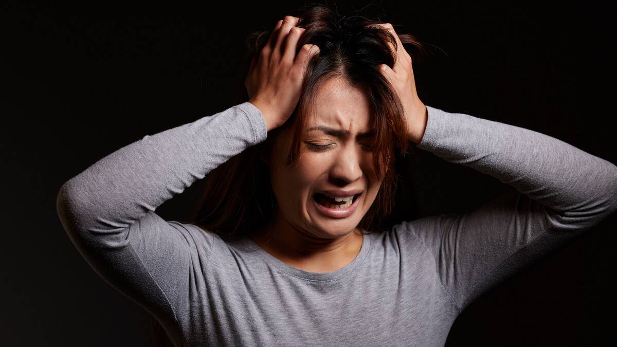 A woman crying in distress with her hands in her hair.