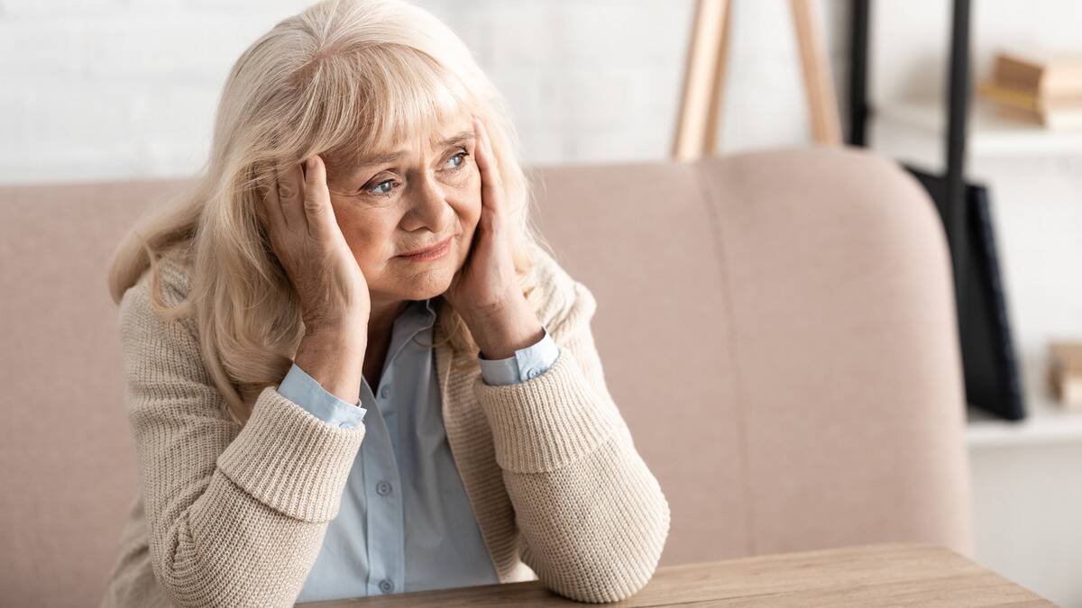 A woman sitting with both of her elbows on the table, a hand on either side of her face as she looks off to the side.