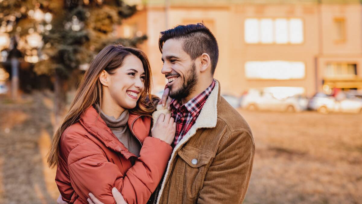 A couple walking outside during autumn, arms around one another as they smile.