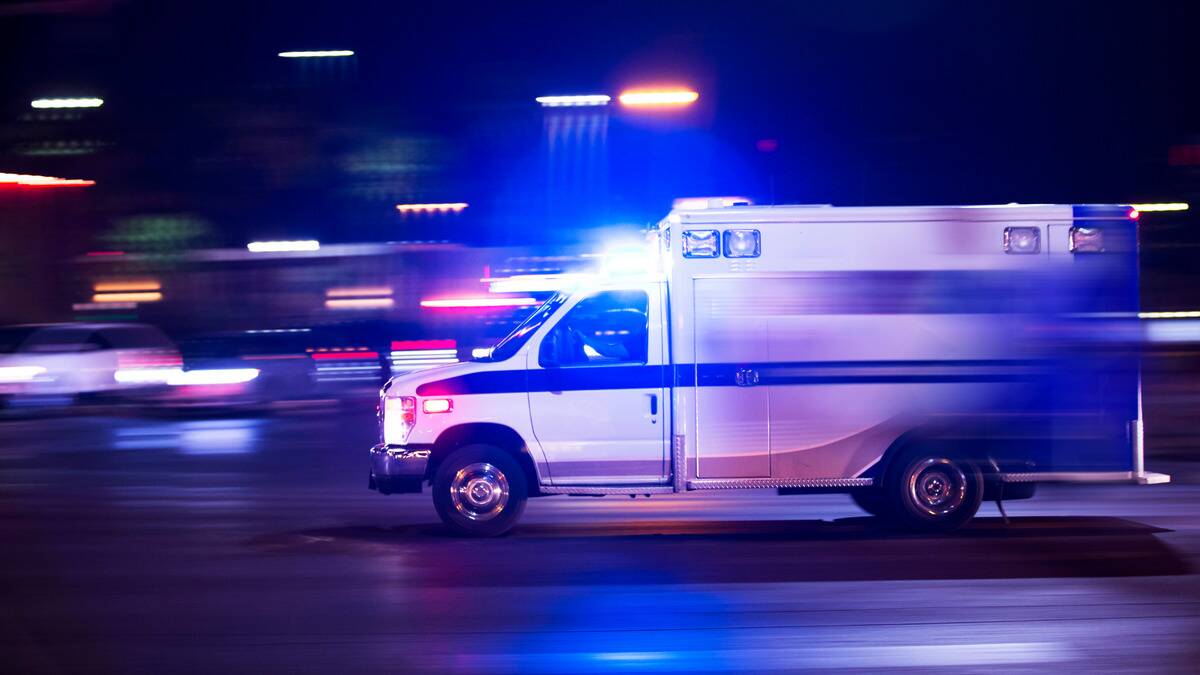 An ambulance rushing through the street at night, lights blinking.