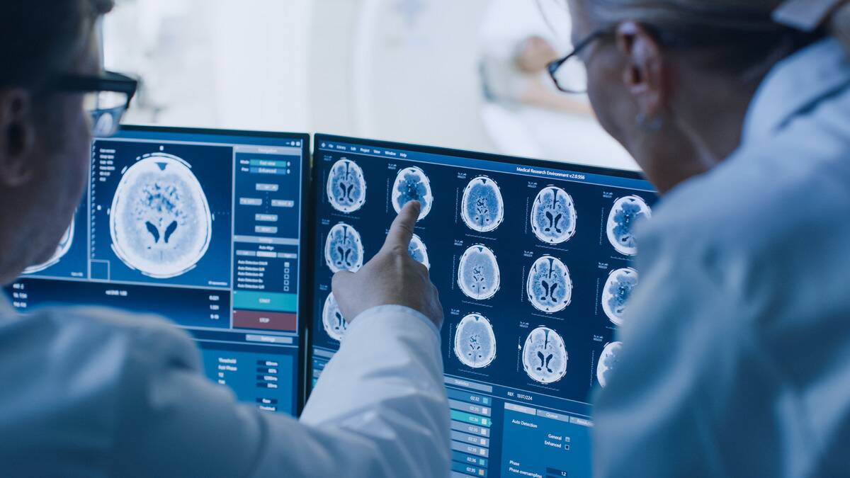 A pair of doctors examining and pointing at a series of brain scan images.