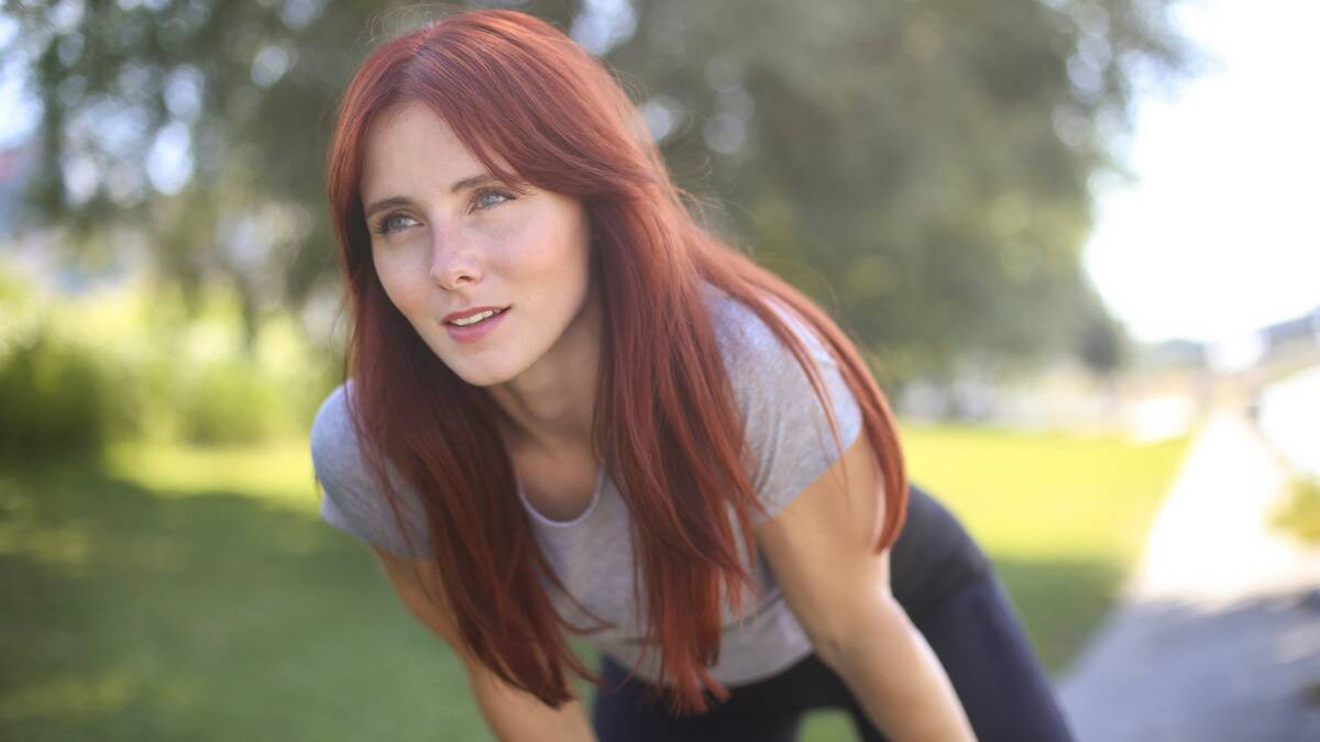 A woman leaning forward, hands on her knees, looking forward with a determined expression.