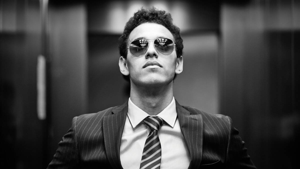 A greyscale image of a confident looking business man wearing sunglasses.