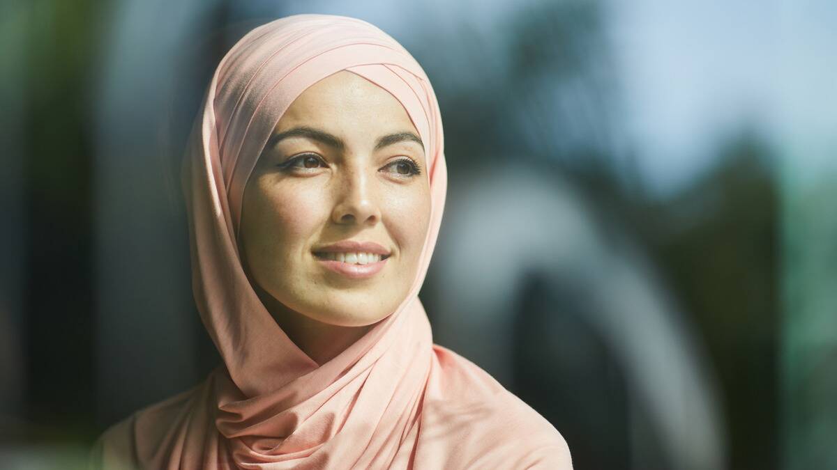 A woman in a pink headscarf smiling gently as she looks out to the side.