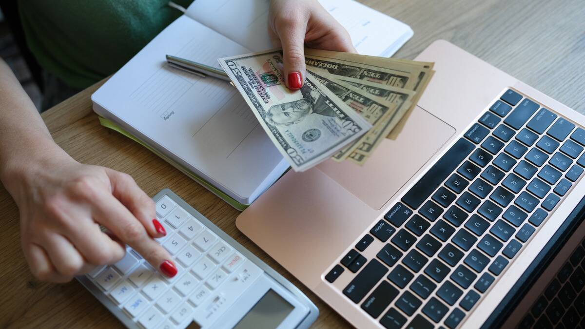 An above shot of someone counting a stack of bills while punching numbers into a calculator.