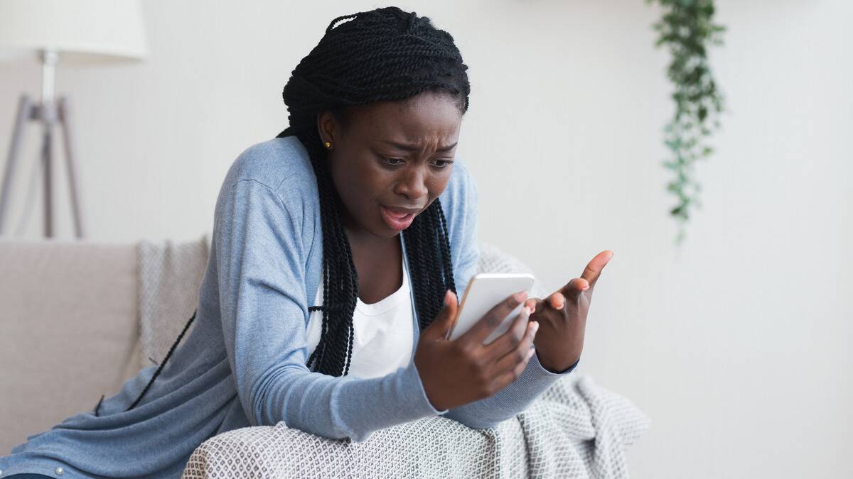 A woman holding her phone and looking at it with a shocked, confused expression. 