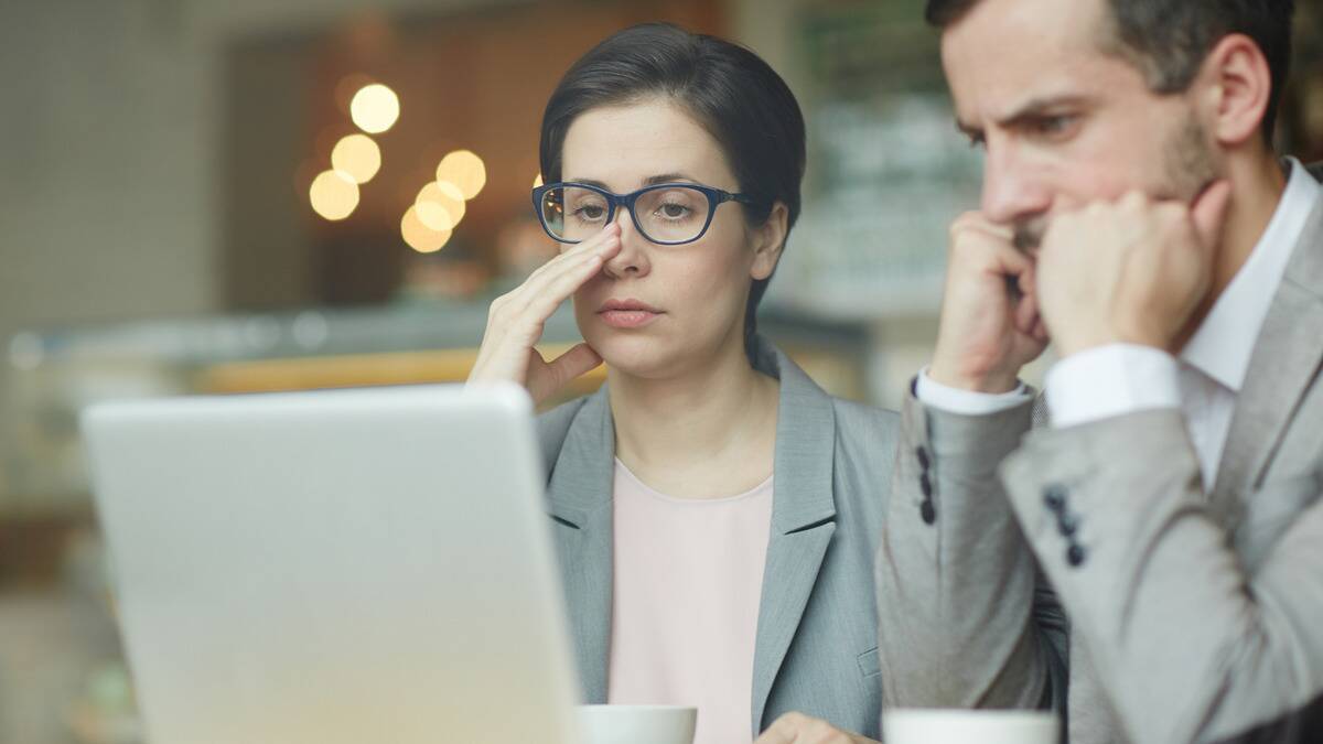 A woman and a man at work, both looking frustrated as they watch the same laptop.