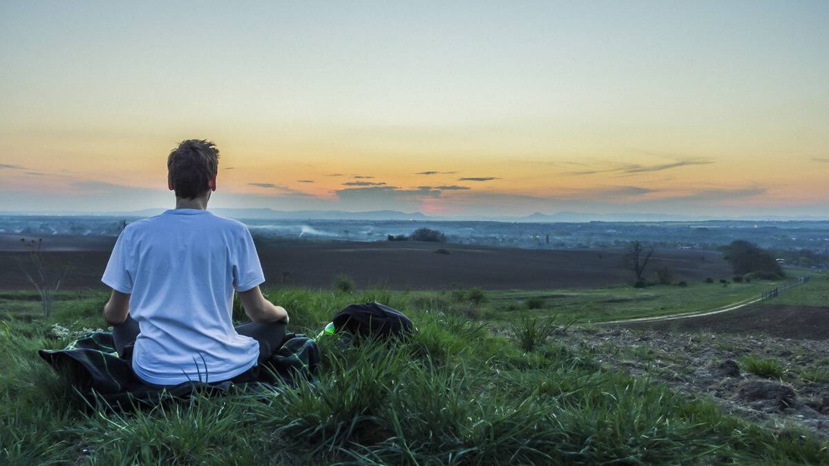 A man sitting in a grassy field looking out at the horizon as the sun rises.