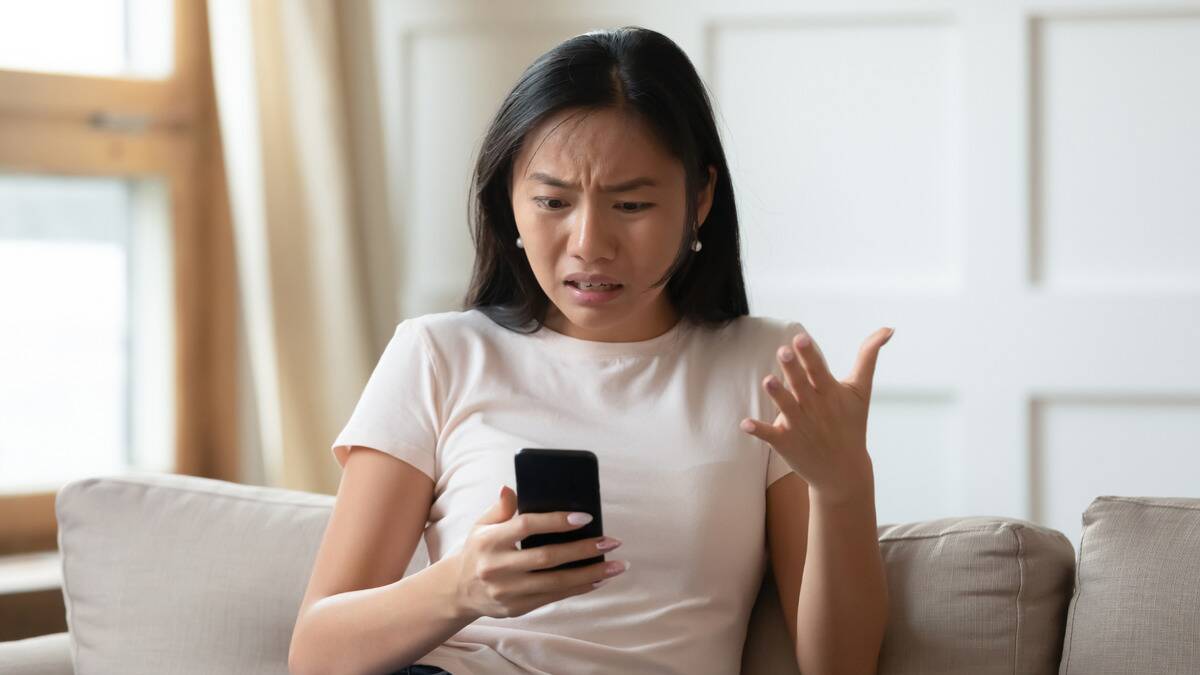 A woman looking at her phone with a confused and frustrated expression.