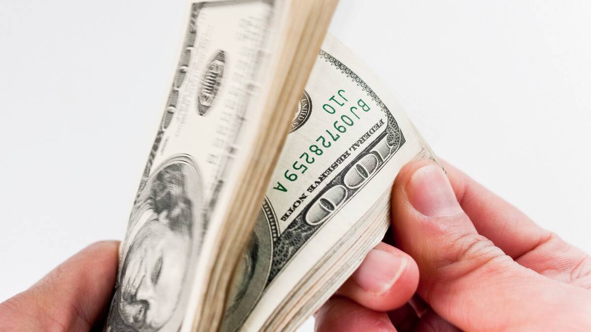 A close shot of a pair of hands flipping through a stack of $100 bills.