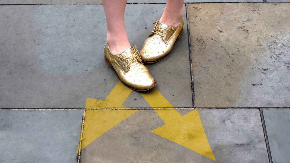 Two arrows painted on the sidewalk pointing in slightly different ways, someone's feet in golden shoes standing before them.