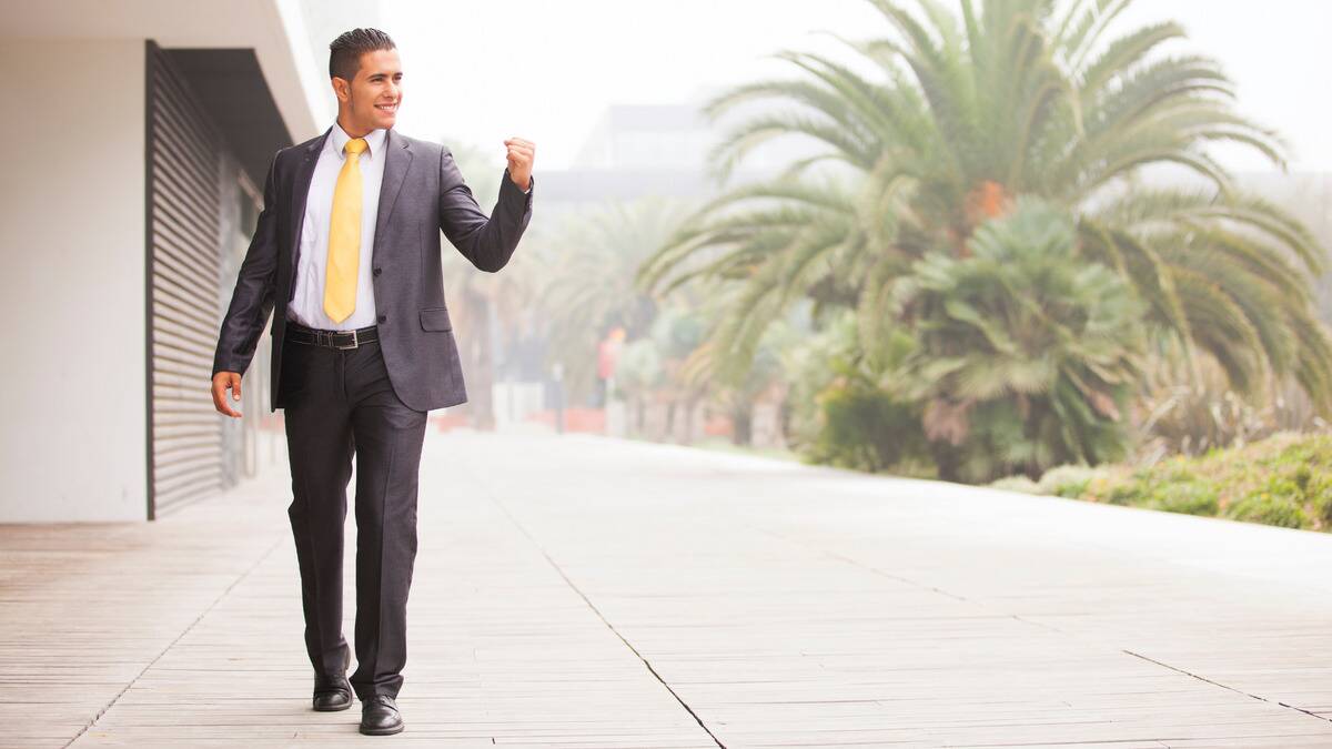 A man in a business suit walking outside, a fist up, looking confident.