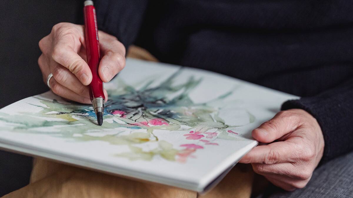 A close shot of someone drawing over a watercolor painting in a small sketchbook.