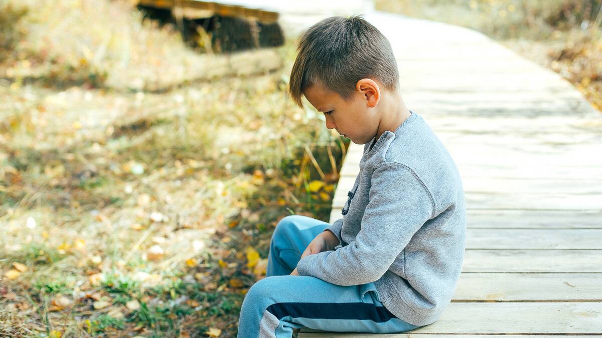 A young boy sitting outside, looking sad.