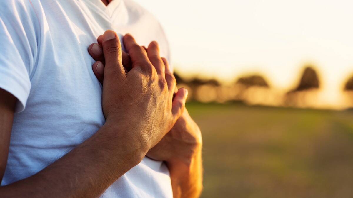 A close shot of a man's chest with both hands over his heart.