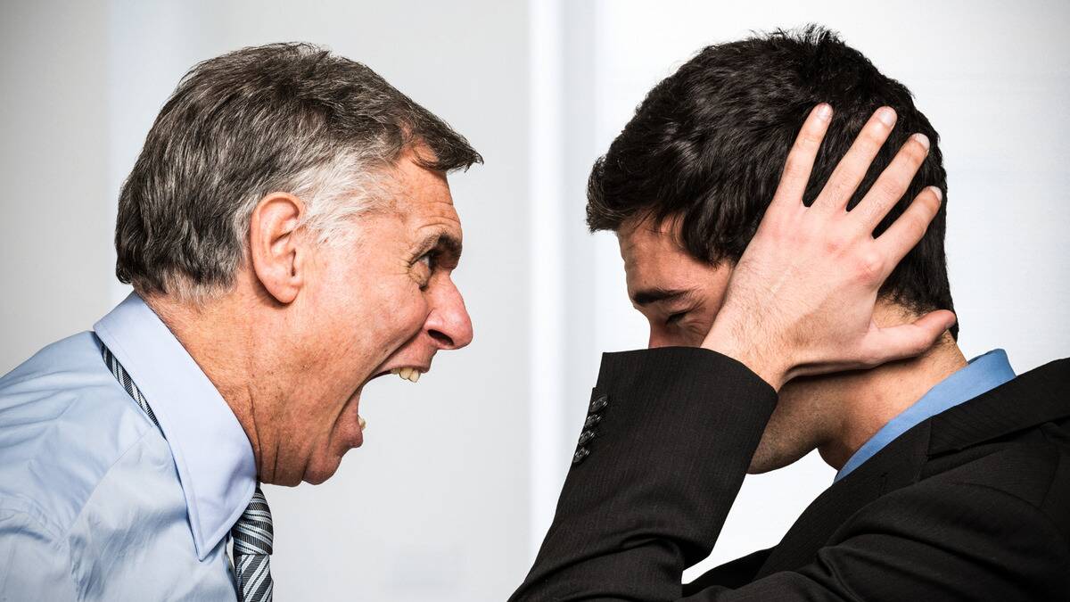 A man being yelled at by his angry boss, covering his ears with his hands.