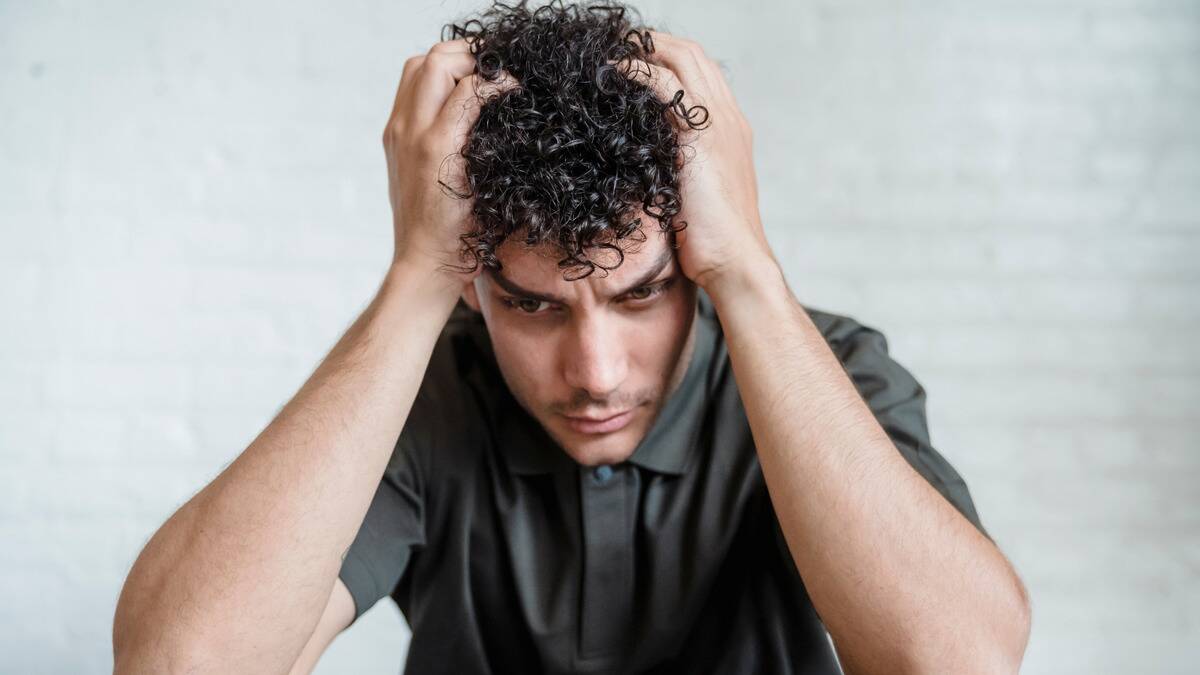 A man sitting at a table, hands in his hair, leaning forward with a sad expression.