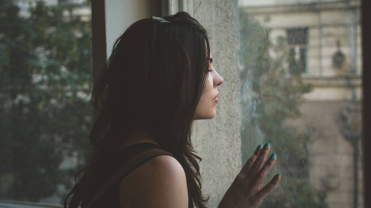 A woman looking out the window at the streets below forlornly.