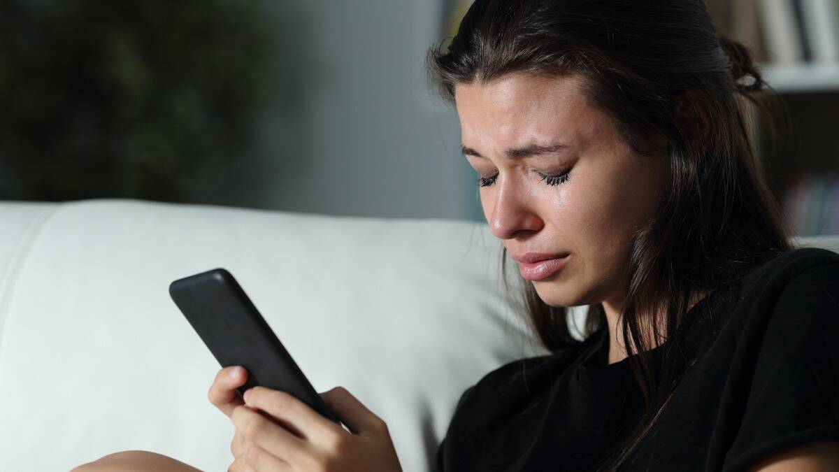 A woman with her eyes closed, crying as she holds her phone up.