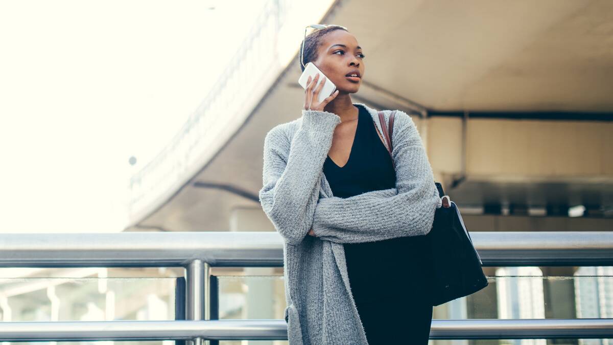 A woman speaking on the phone as she leans against a railing outside, looking off to the side.