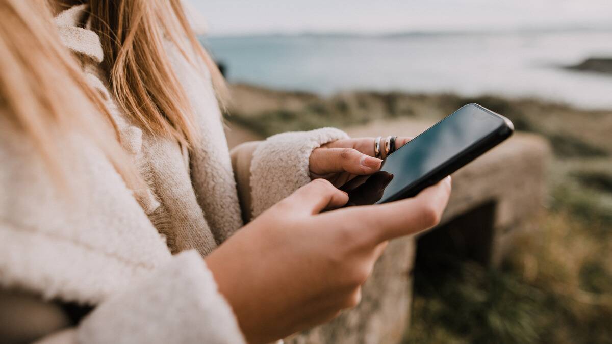 A woman texting on her phone while standing outside, the focus on her hands holding the phone.