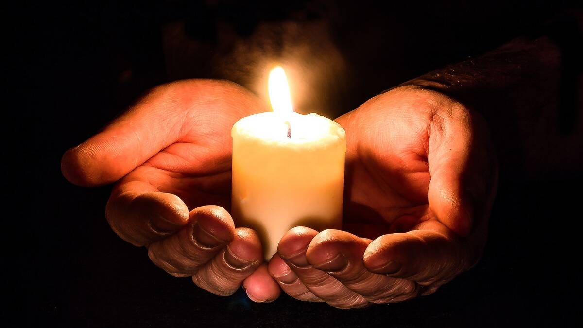 A close shot of a pair of cupped hands holding a candle.