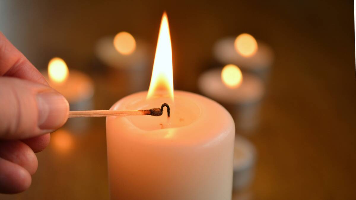 A close shot of someone lighting a large candle with a match.