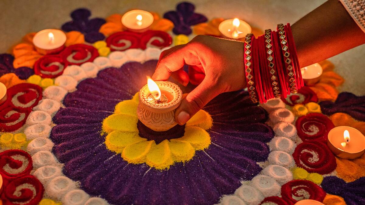 Someone placing a candle in the center of a mandala made with colorful sand.