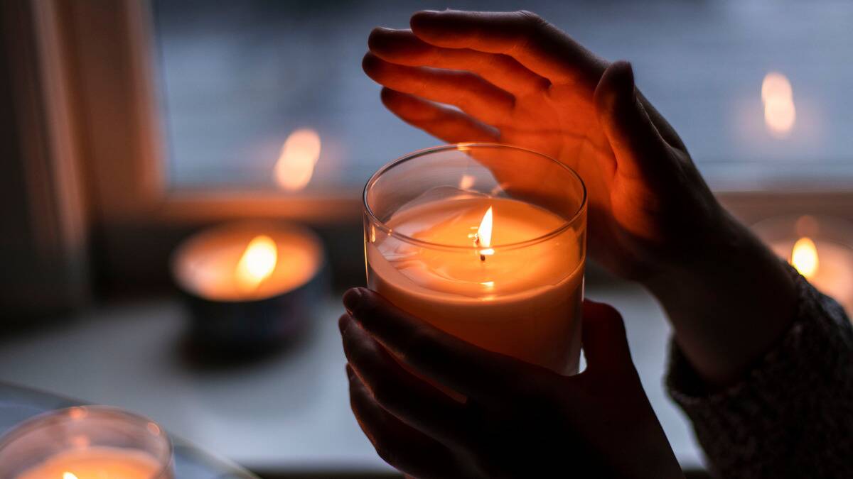 Someone holding a candle in a class container with one hand, the other hand sheltering the flame.