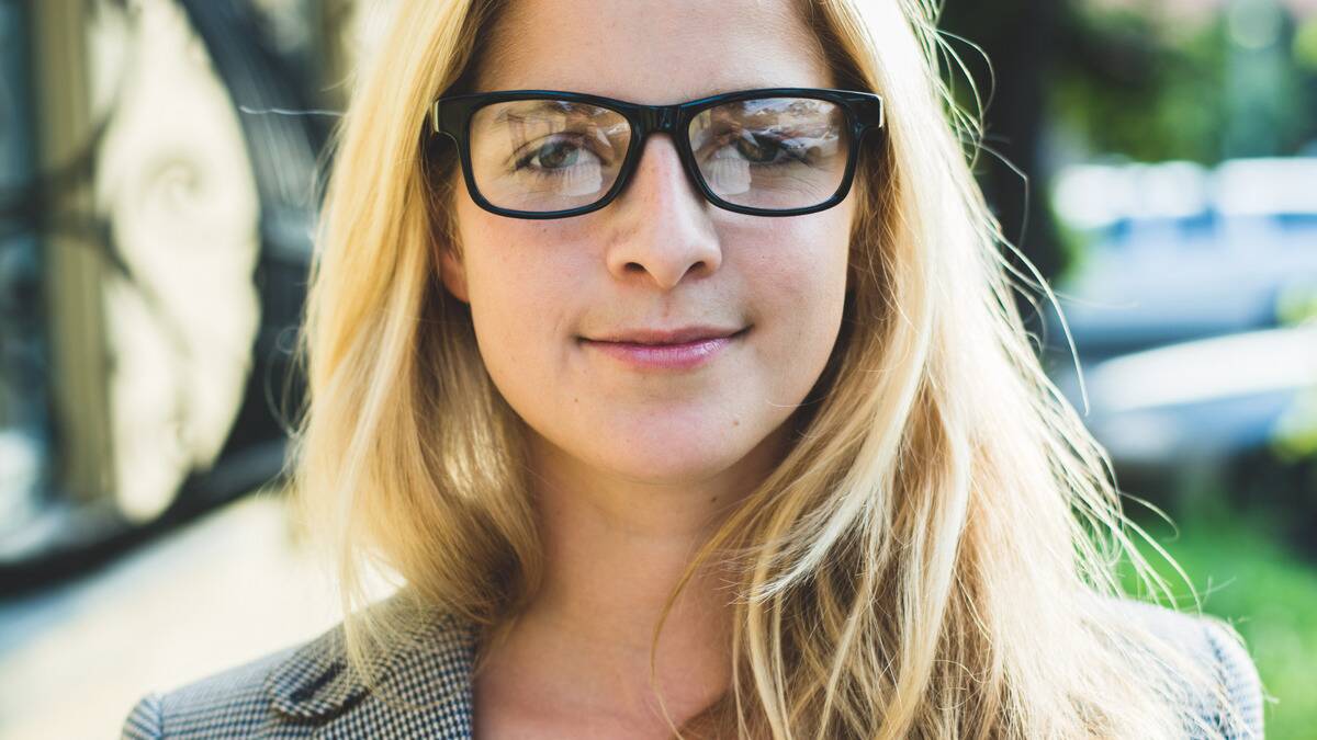 A close shot of a woman in glasses staring forward confidently.