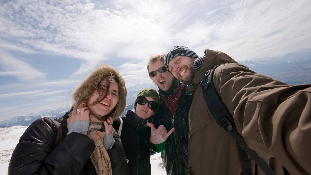 A low angle selfie shot of a group of friends who are hiking during winter, all smiling and posing for the camera.