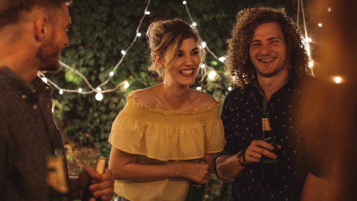 Some friends standing outside for a get together, all smiling, holding drinks.