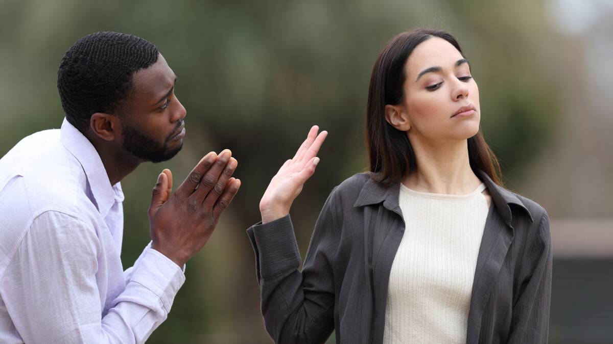 A man pleading to a woman as she holds her hand up to him, shutting him down as she walks past.