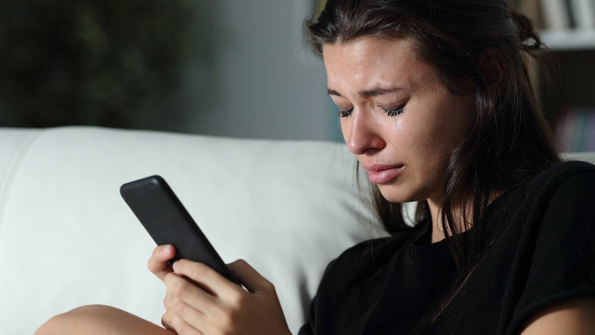 A woman crying with her eyes closed as she holds her phone.