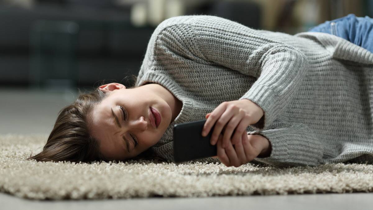 A woman laying on her side on the floor, looking at her phone sadly.