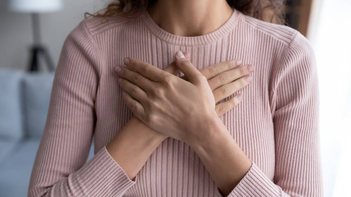 A woman with both hands folded over the center of her chest.